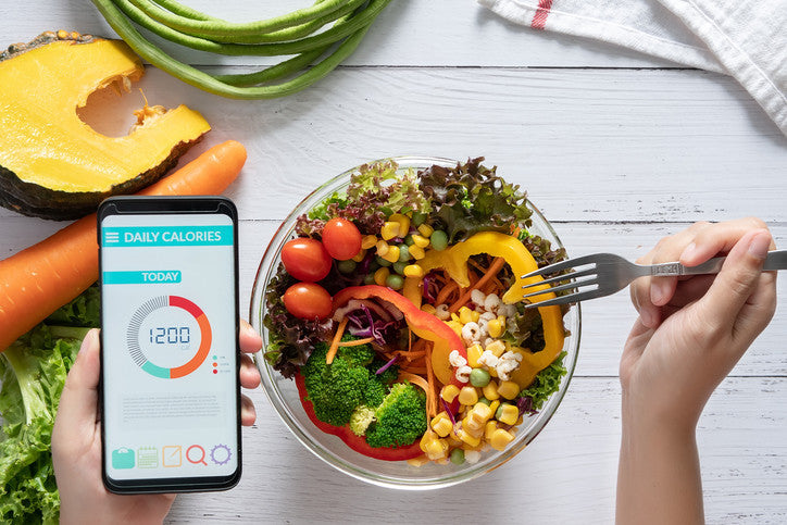 Person Eating Fruits And Veggies While Looking A Calories On Their Phone