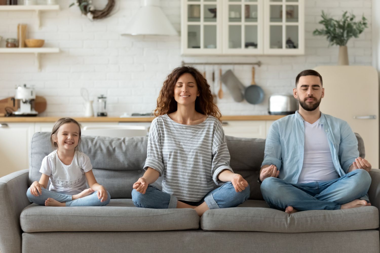 Two Parents And Their Young Daughter Meditating On The Couch
